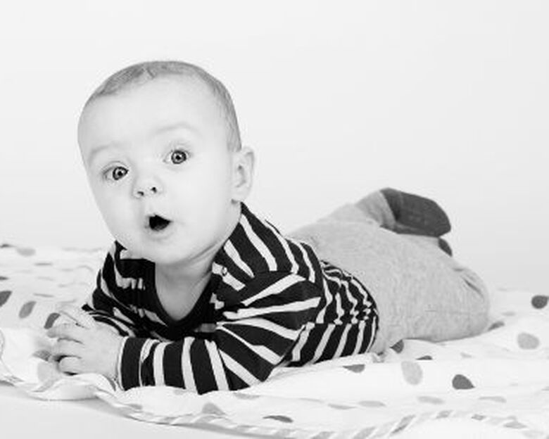 En baby ligger på maven på et rundt tæppe med prikker og kigger ud i luften.