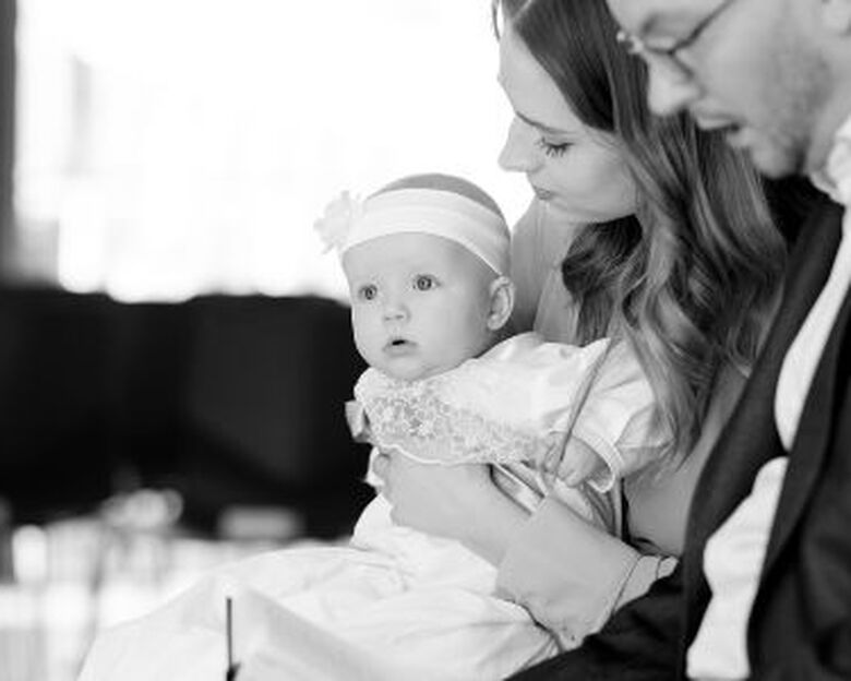 en baby i dåbskjole sidder ved sin mor i kirken