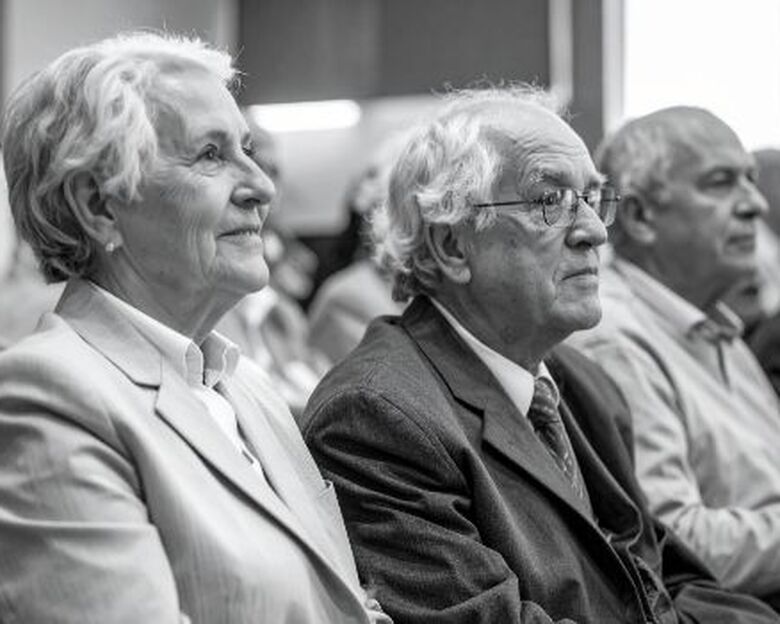 Tre ældre mennesker sidder og lytter til et foredrag (AI-genereret)