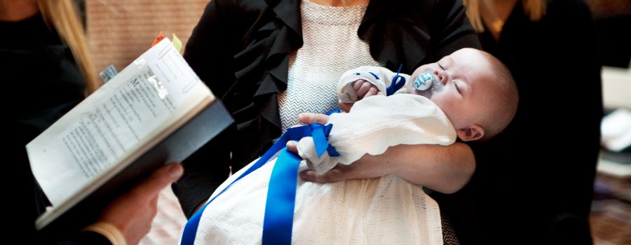 En baby i dåbskjole ligger ved siden mor, og i forgrunden ses en salmebog