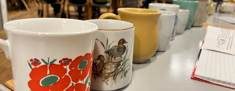 Forskellige krus st&aring;r i en lang r&aelig;kke p&aring; kanten af et bord 